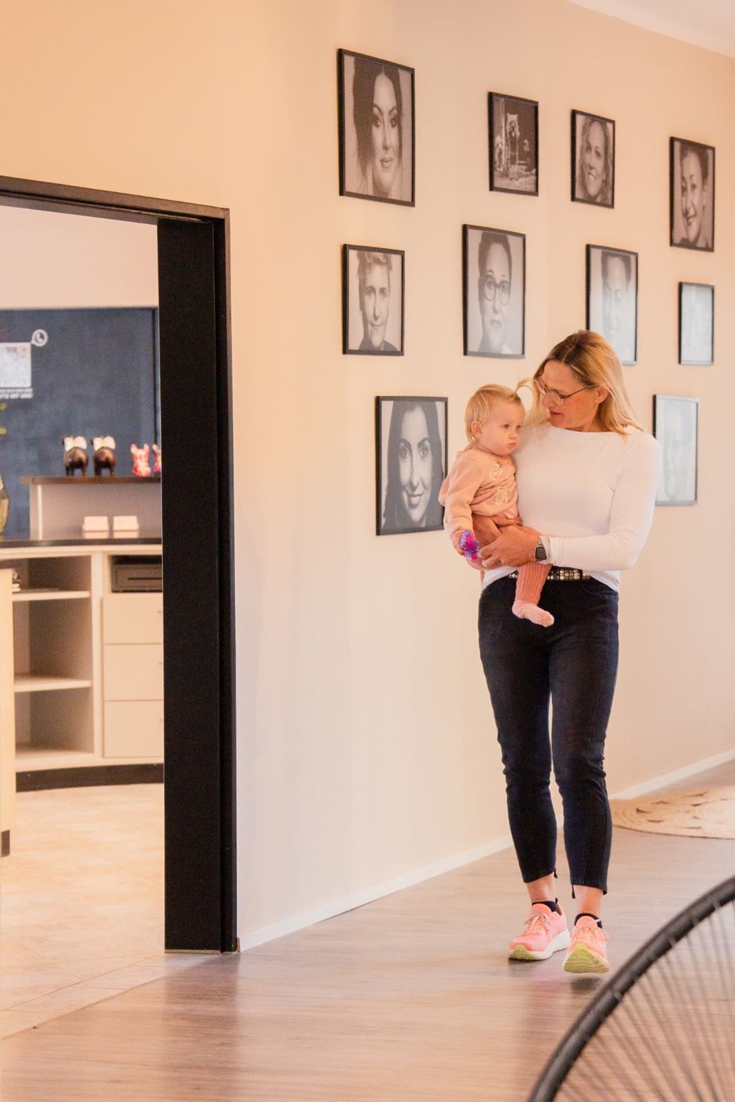 Frau mit Kleinkind im Flur vor der Wand mit Portraits